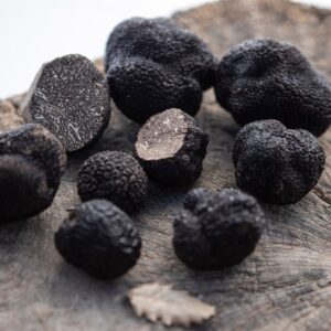 Some black truffles over a wooden surface and an oak leaf